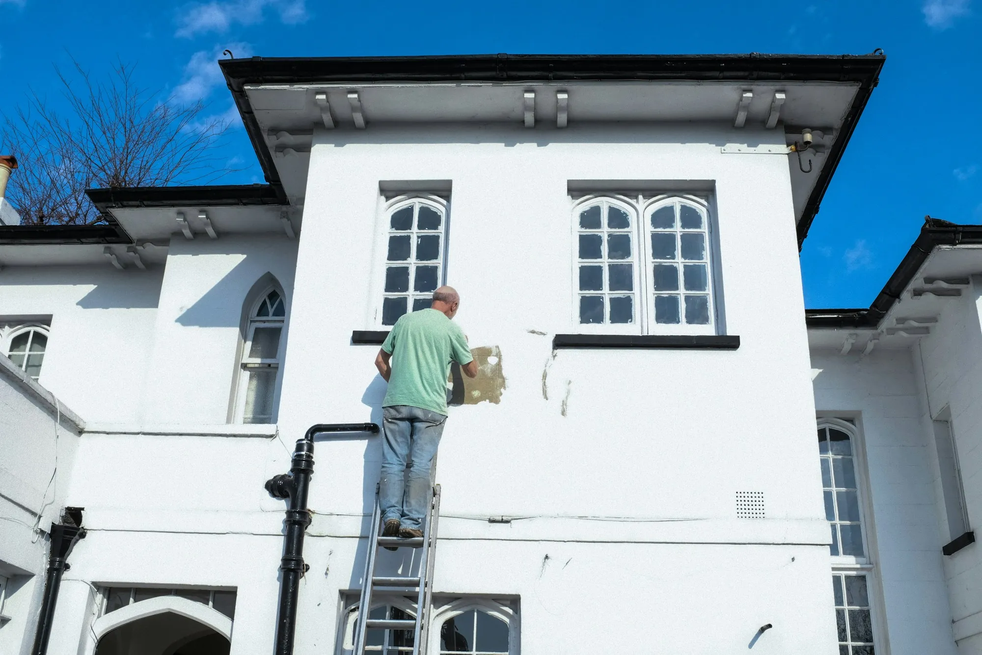 Worker on a ladder checking the upper wall of a white house