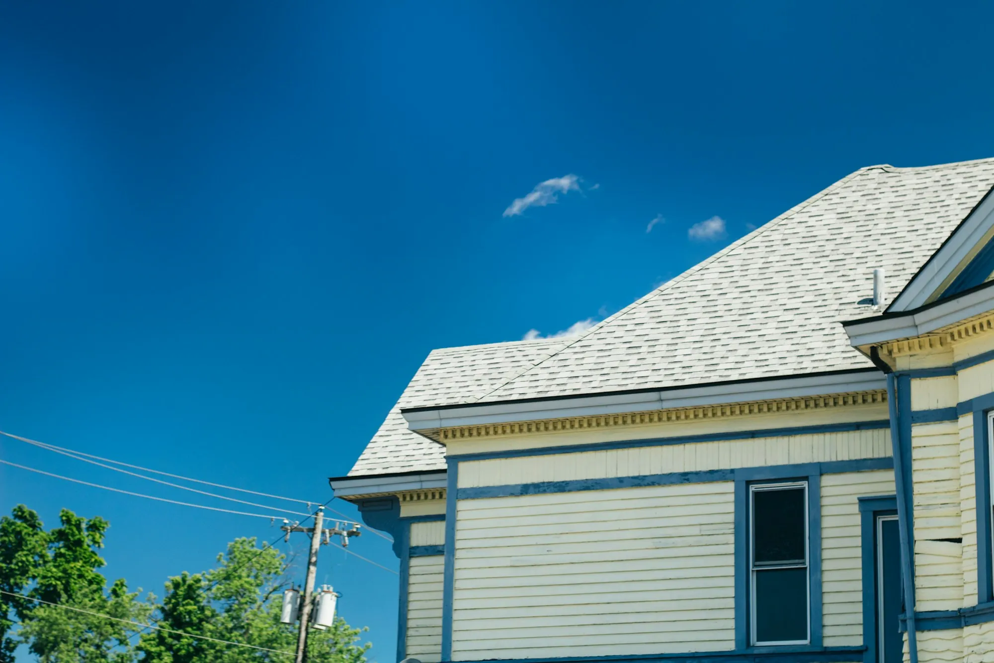 Low-angle view of a light gray shingle roof on a blue-sided Victorian home
