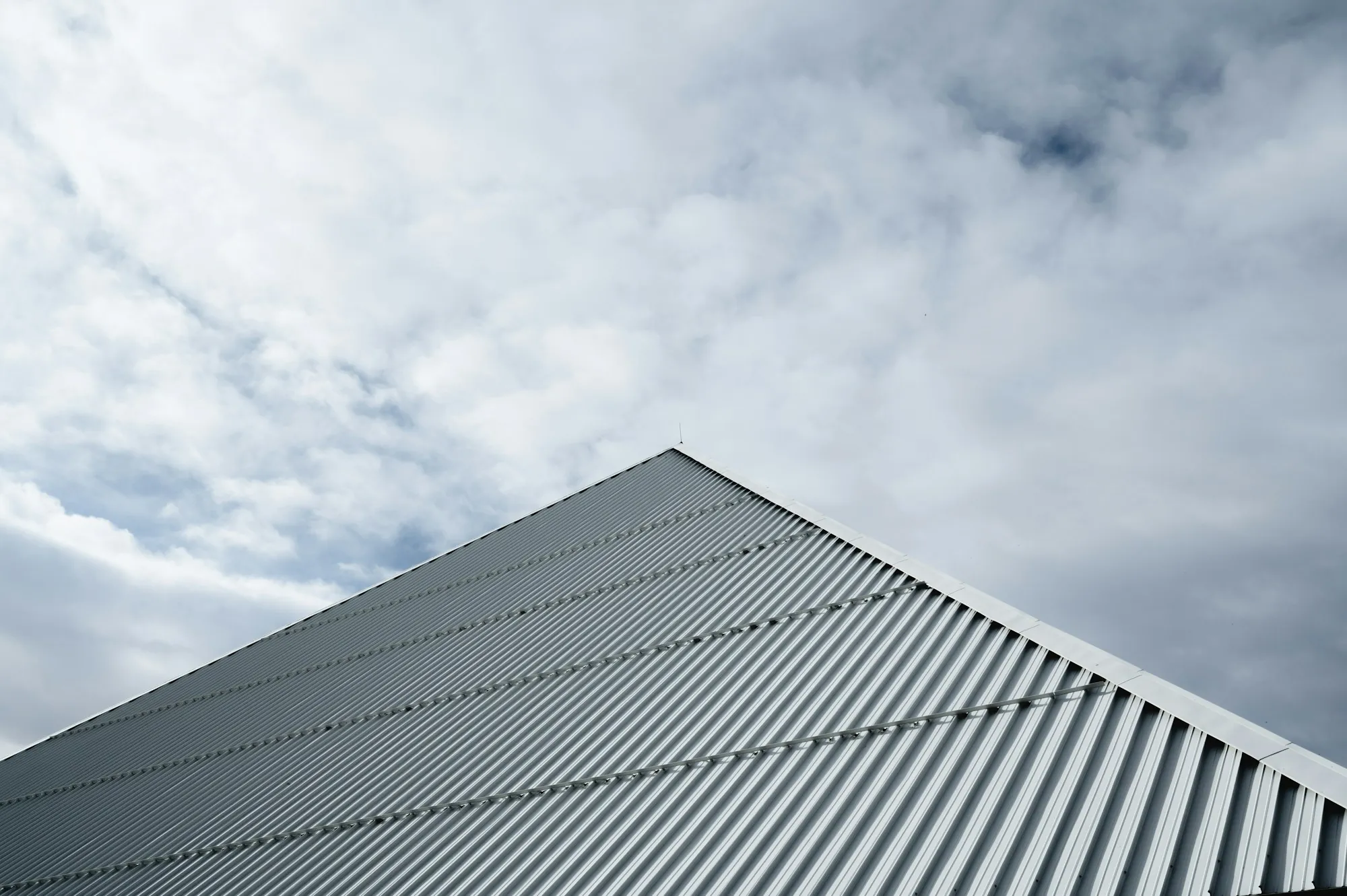 Ribbed metal roof rising against a cloudy sky