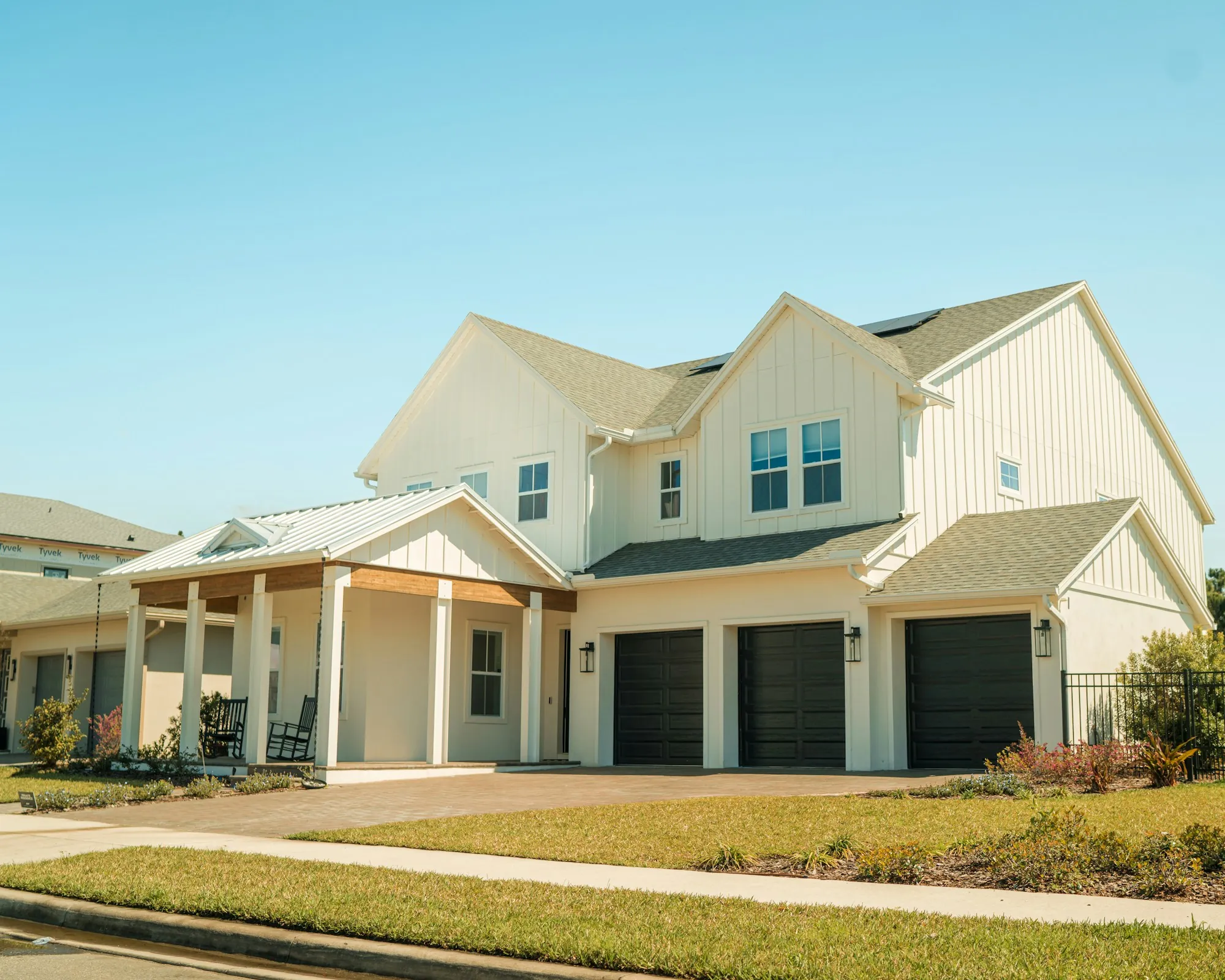 Cream farmhouse-style home with layered shingle roofs and a three-car garage