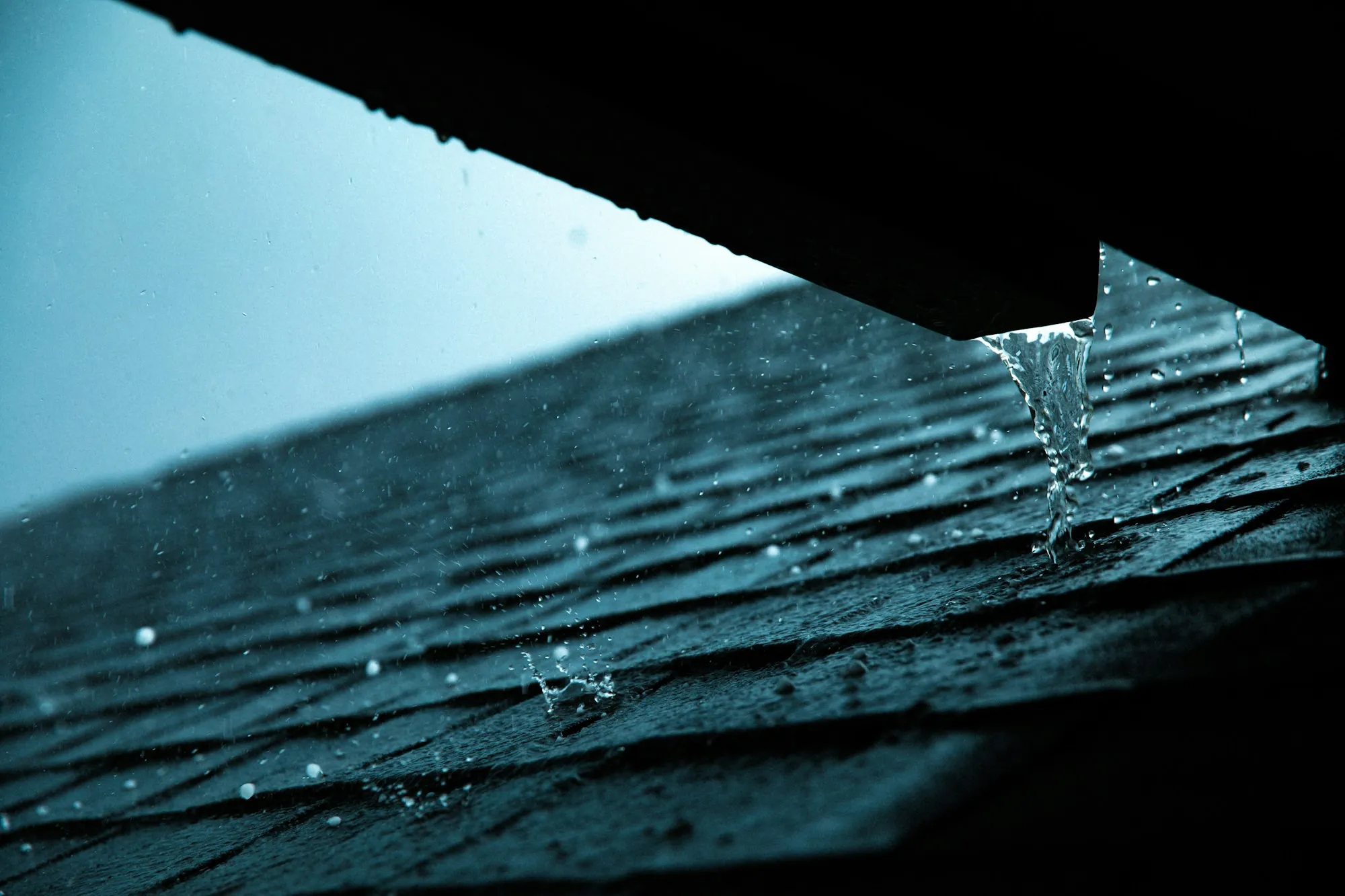 Rainwater dripping off the edge of a shingle roof
