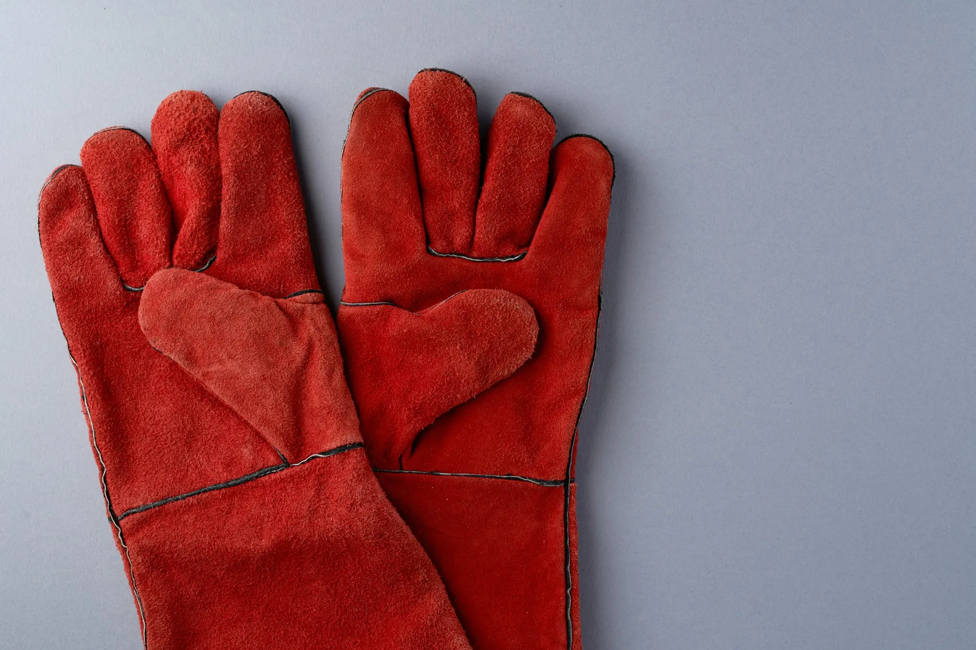 Pair of red leather work gloves on a gray background